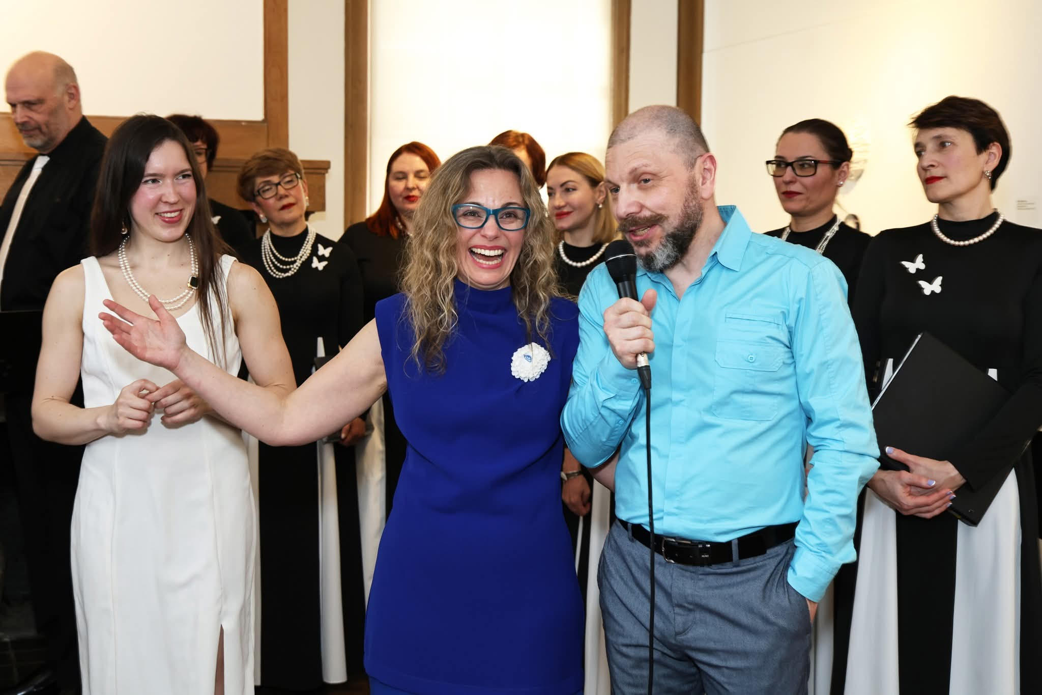 Opening reception with Tanya Besedina and a speaker at the microphone, AVE Choir members in black and white behind them